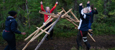 Neljä partiolaista juhlistaa puisen rakennelman valmistumista yhdessä metsässä.
