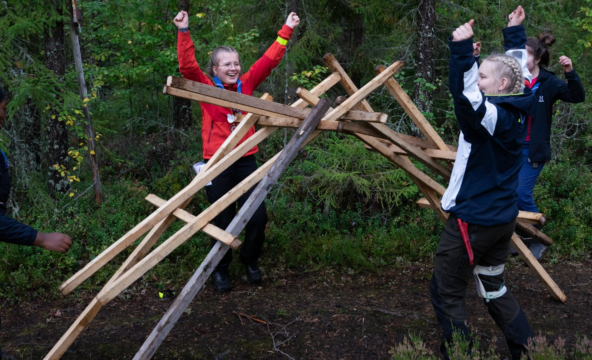 neljä partiolaista juhlistaa puisen rakennelman valmistumista yhdessä metsässä