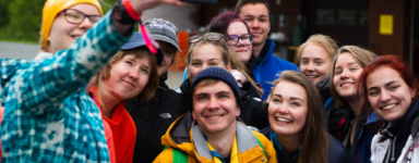 ryhmä iloisia nuoriapartiolaisia värikkäissä vaatteissa ottamassa selfietä