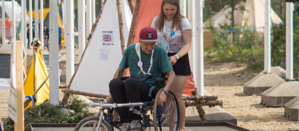 Partiolainen auttaa toista liikkumaan rampilla pyörätuolilla leirillä