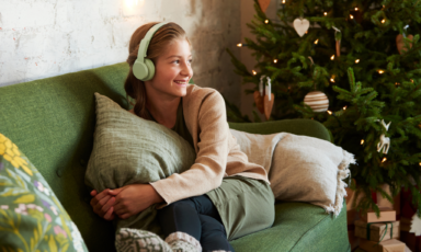 Tyttö sohvalla kuulokkeet päässään ja taustalla joulukuusi.