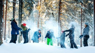 Ryhmä ihmisiä talvisessa metsässä heittämässä lunta ilmaan.
