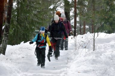 Ryhmä partiolaisia kävelee jonossa lumisella tiellä.