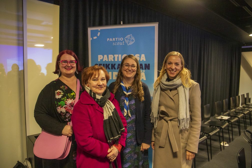 Keskusteluun osallistuneet kansanedustajat yhteiskuvassa partion roll-upin edessä. Vasemmalta oikealle: Pia Lohikoski, Anne Kalmari, Inka Hopsu (partiohuivi) ja Sandra Bergqvist.
