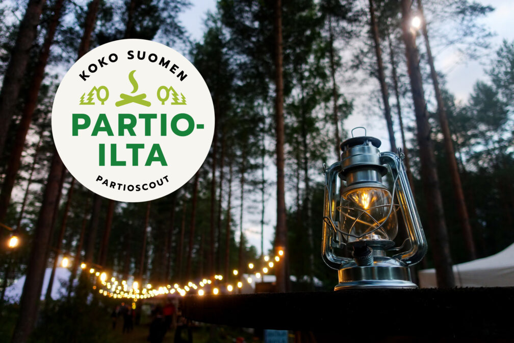 Koko Suomen partioillan tunnus sekä lyhty ja valoja metsässä.